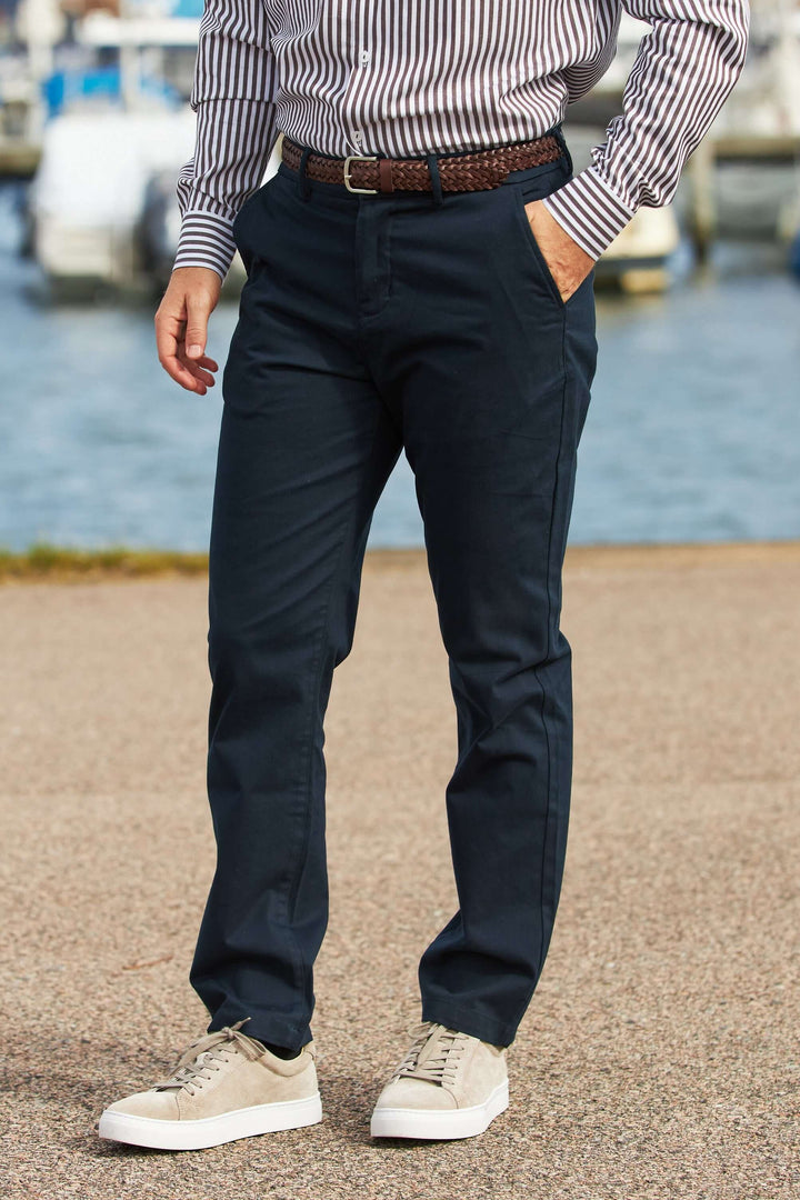 En man i marinblå Stretch Chinos och randig skjorta, står vid vattnet.