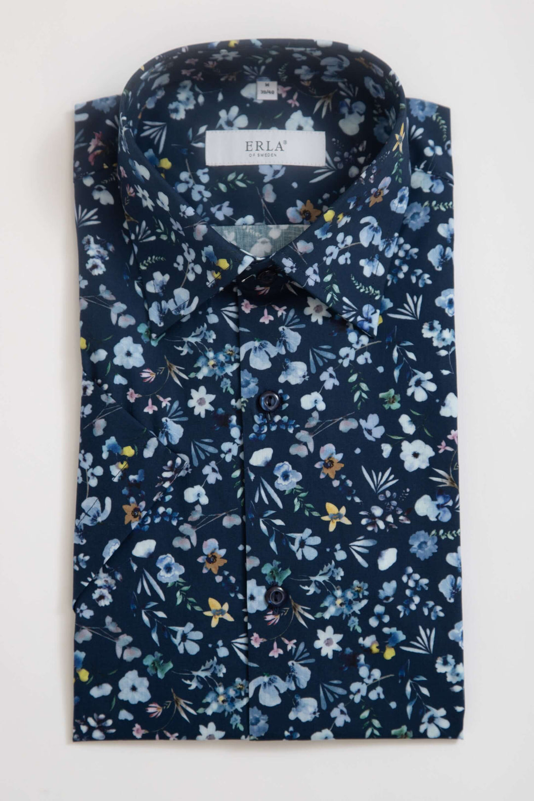Mörkblå kortärmad skjorta med blommigt mönster liggande på en vit yta.