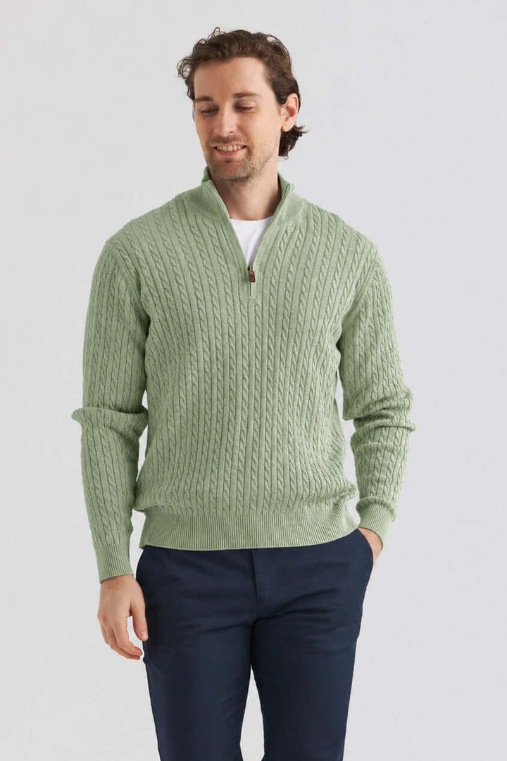Grön kabelstickad tröja half zip på man som bär en stilren tröja med dragkedja och kabelstickning.