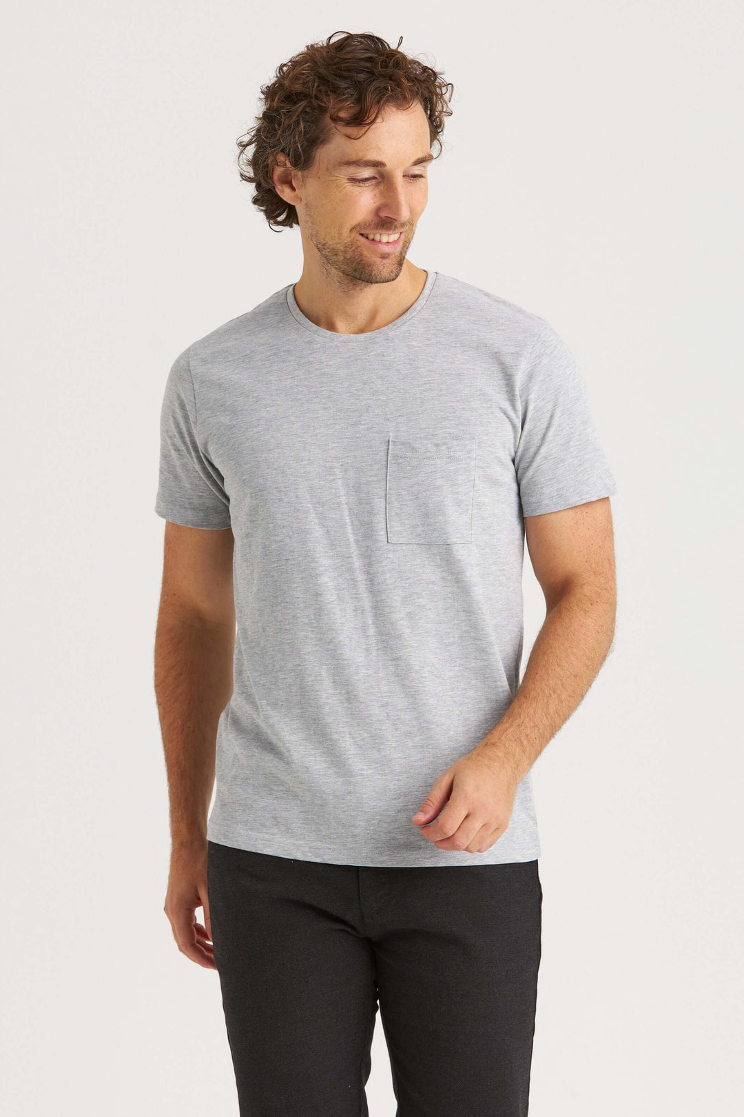 Man wearing an original gray T-shirt with a pocket, smiling against a plain background.