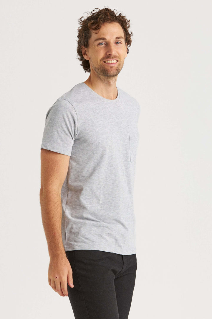 Model wearing a gray original T-shirt with a pocket, styled with black pants, smiling against a clean background.