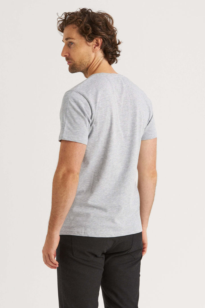 Man wearing a gray original T-shirt, shown from the back, styled with black pants against a plain backdrop.