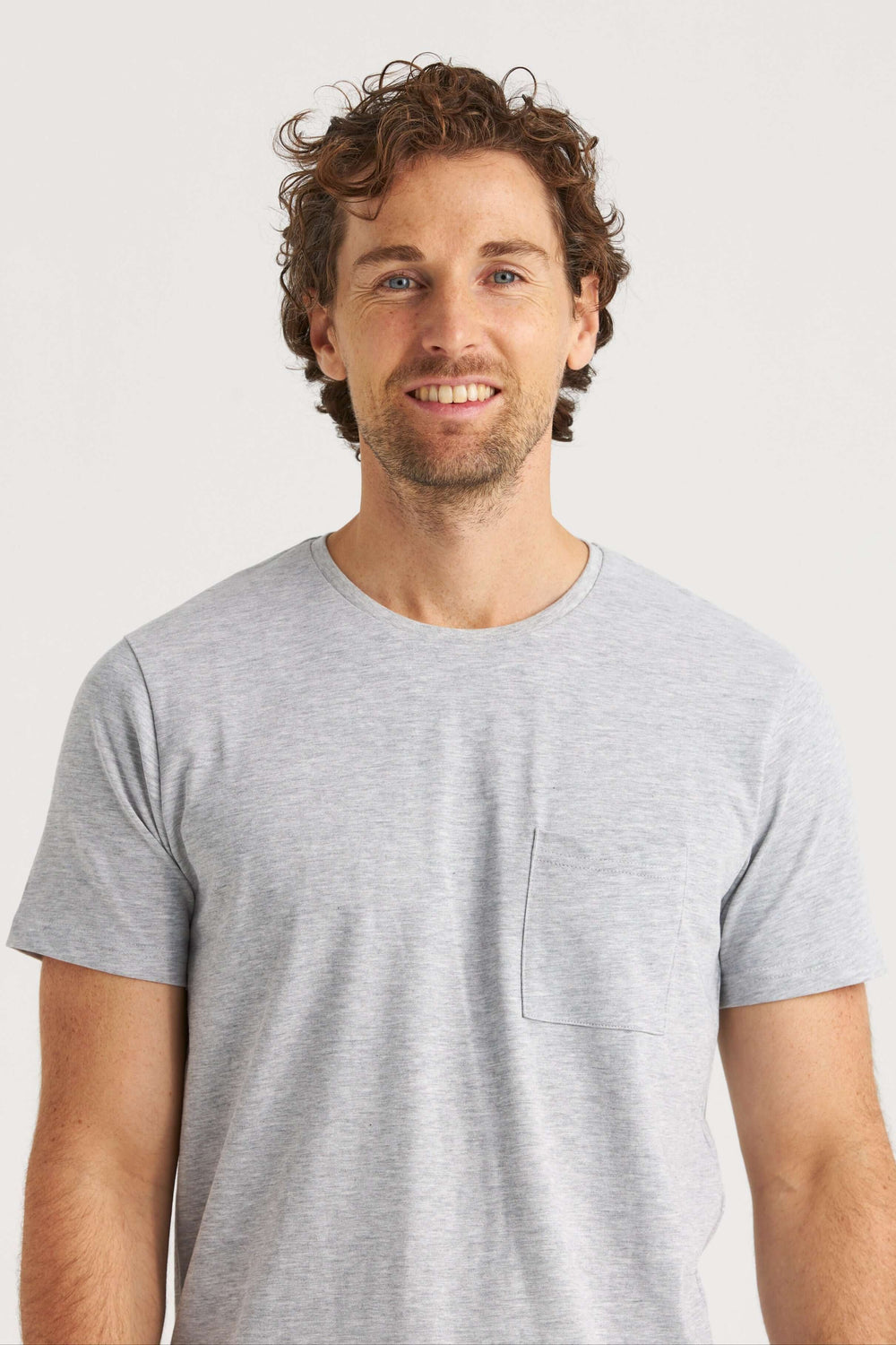 Man wearing a gray original T-shirt with a pocket on the left chest, smiling at the camera.