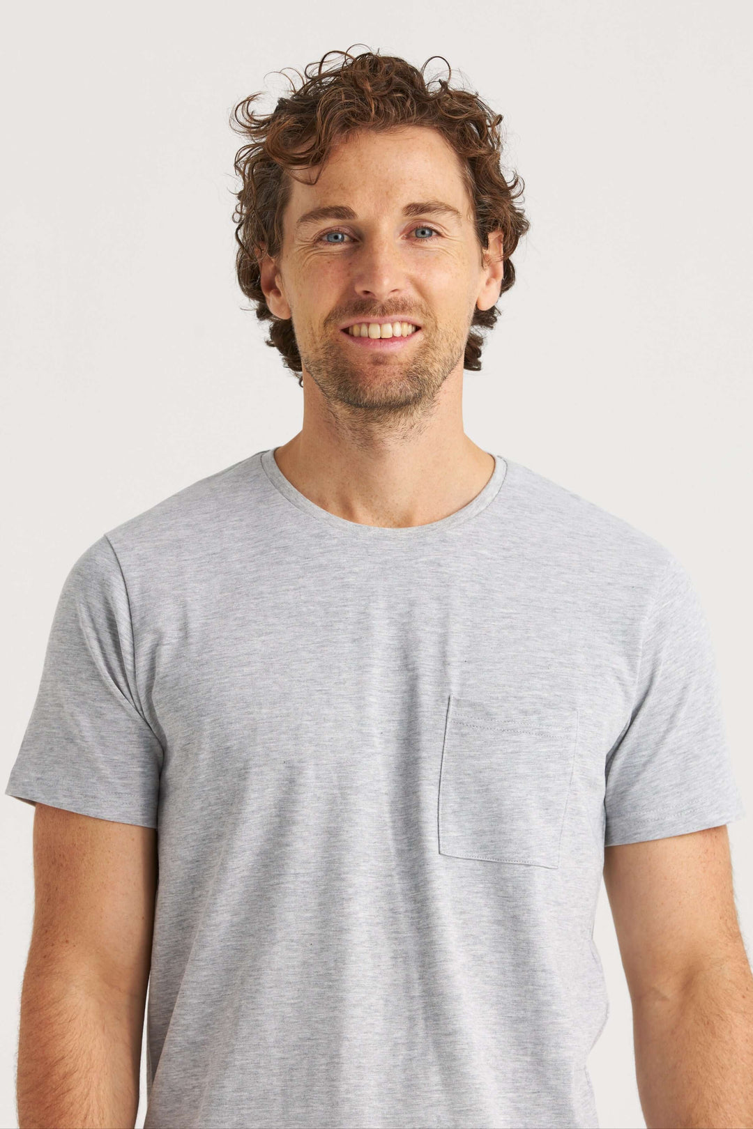 Man wearing a gray original T-shirt with a pocket on the left chest, smiling at the camera.