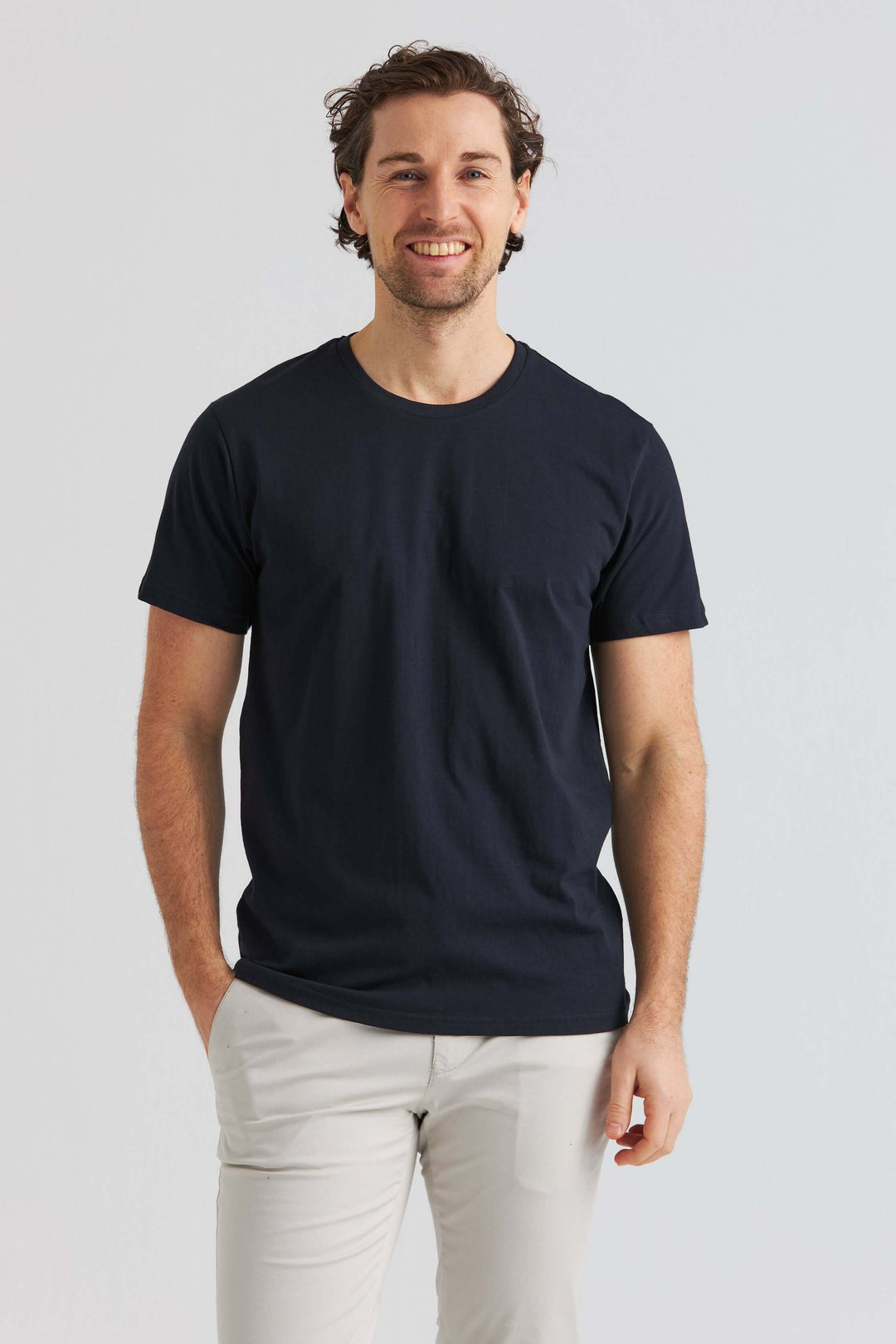 En man i marinblå core t-shirt poserar vänligt med händerna i fickorna.