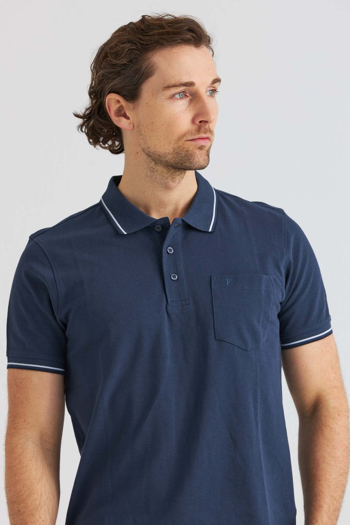 Marinblå Pikétröja med Kontrastdetaljer, man som bär en marinblå pikétröja med vit kontrast på kragen.