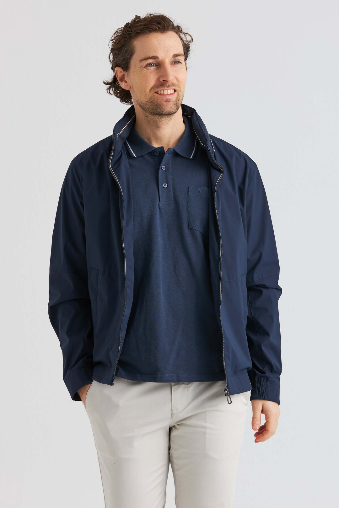 Man som bär Marinblå Lightweight Vårjacka över en polo, stående med ett leende mot en neutral bakgrund.