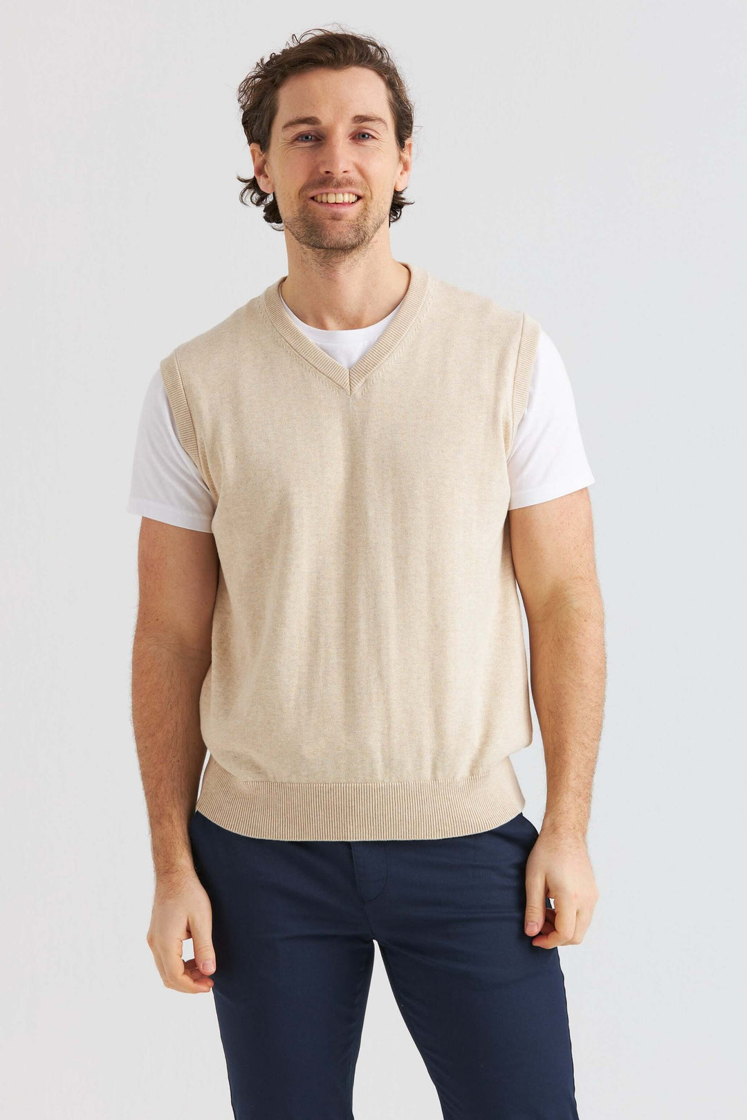 Beige Slipover bärs över en vit t-shirt, perfekt för en avslappnad eller uppklädd look.
