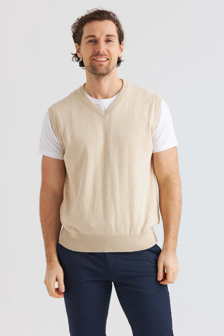 Beige Slipover bärs över en vit t-shirt, perfekt för en avslappnad eller uppklädd look.