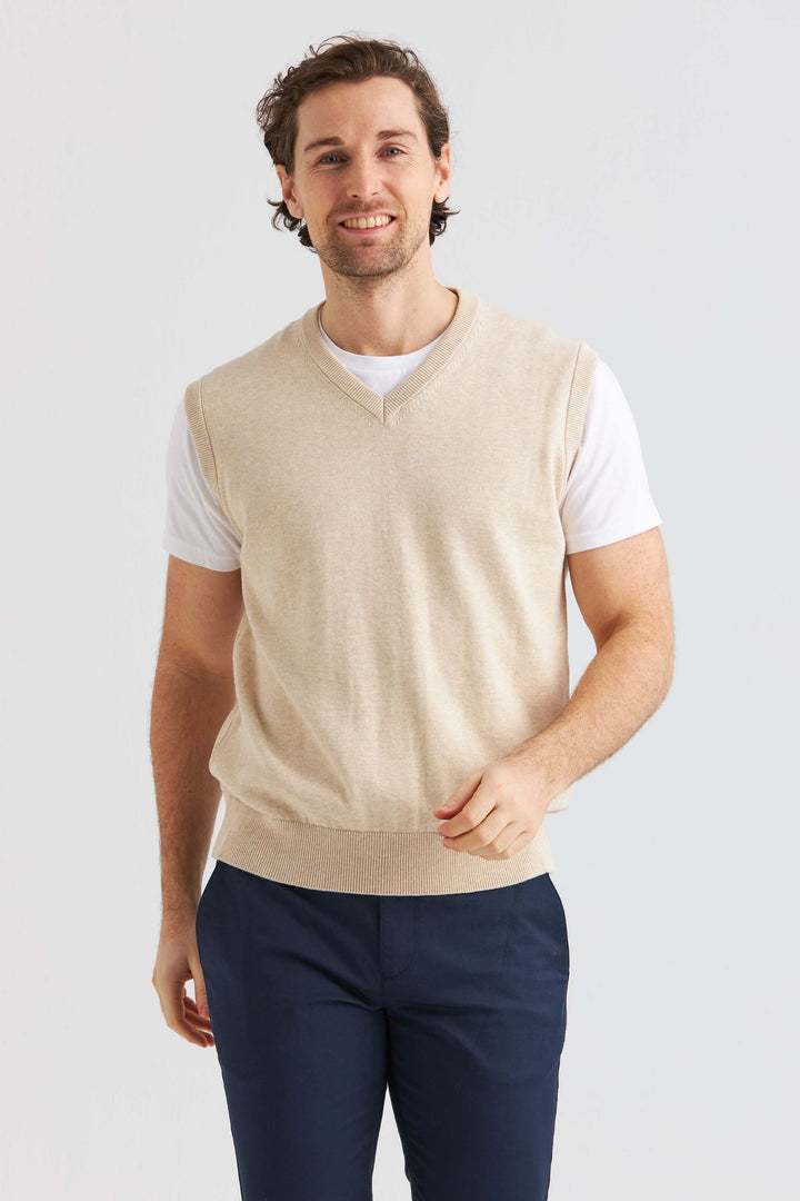 Man bär en beige slipover i mjuk bomull över en vit t-shirt, perfekt för en avslappnad och stilren look.