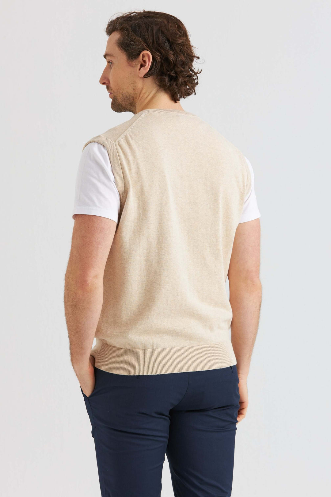 Man som bär en Beige Slipover över en vit t-shirt, sedd från sidan.