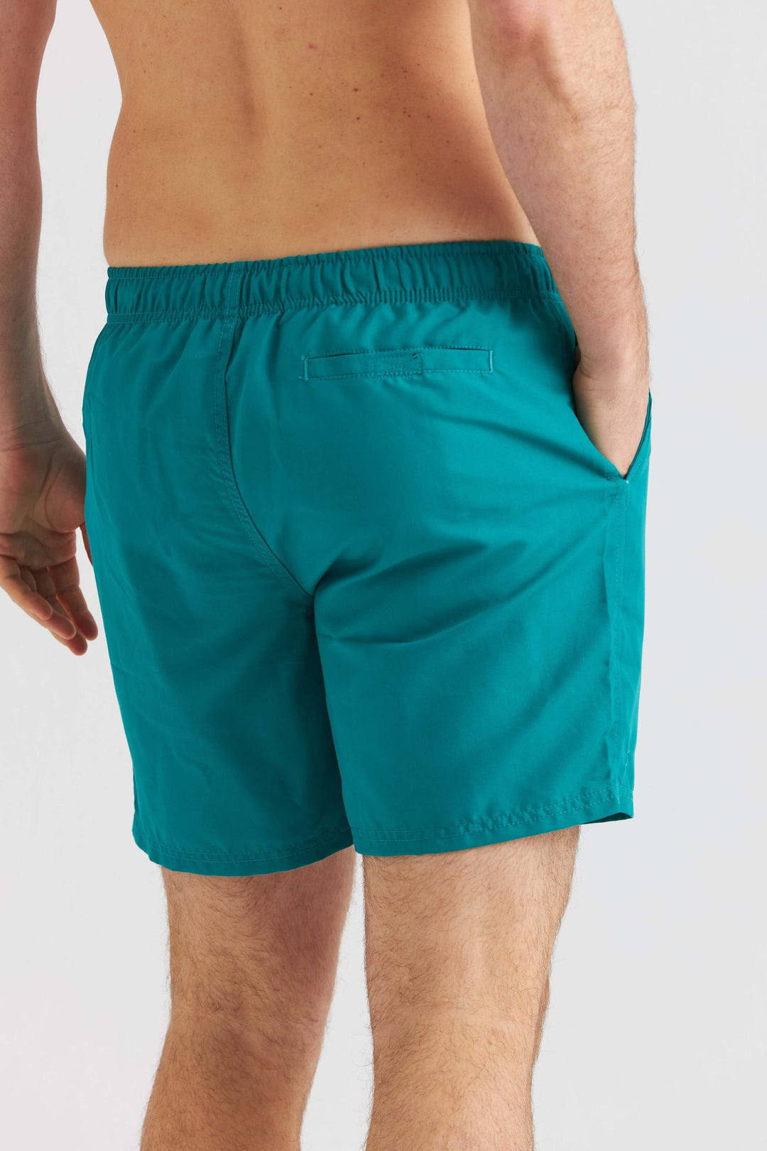 Turkosa badshorts som visar en bakvy av shorts med elastisk midja och fickor.