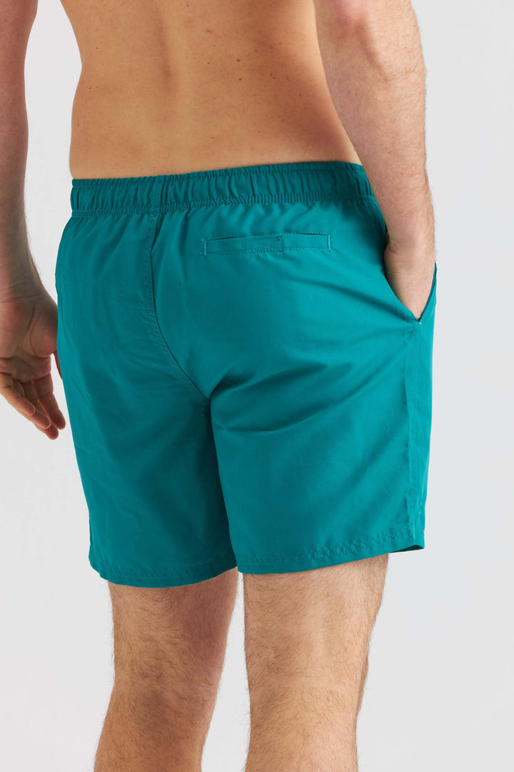 Turkosa badshorts som visar en bakvy av shorts med elastisk midja och fickor.
