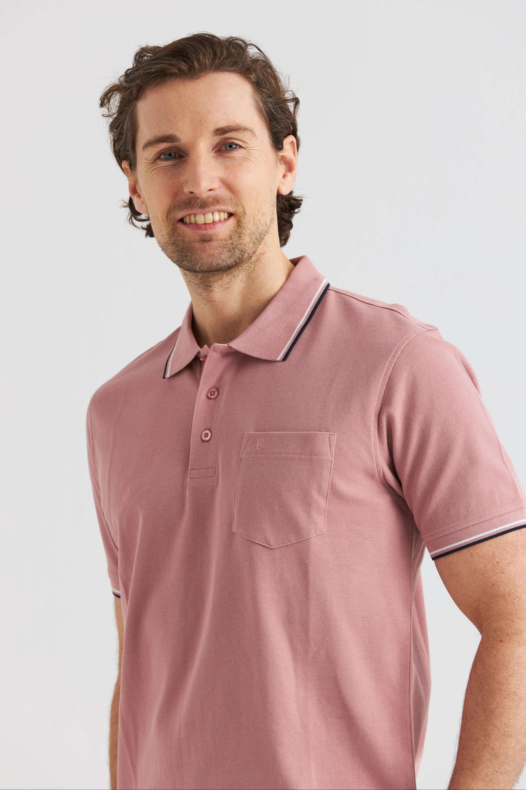 Rosa Pikétröja med Kontrastdetaljer, en man poserar i en rosa pikétröja med detaljer i kontrast.