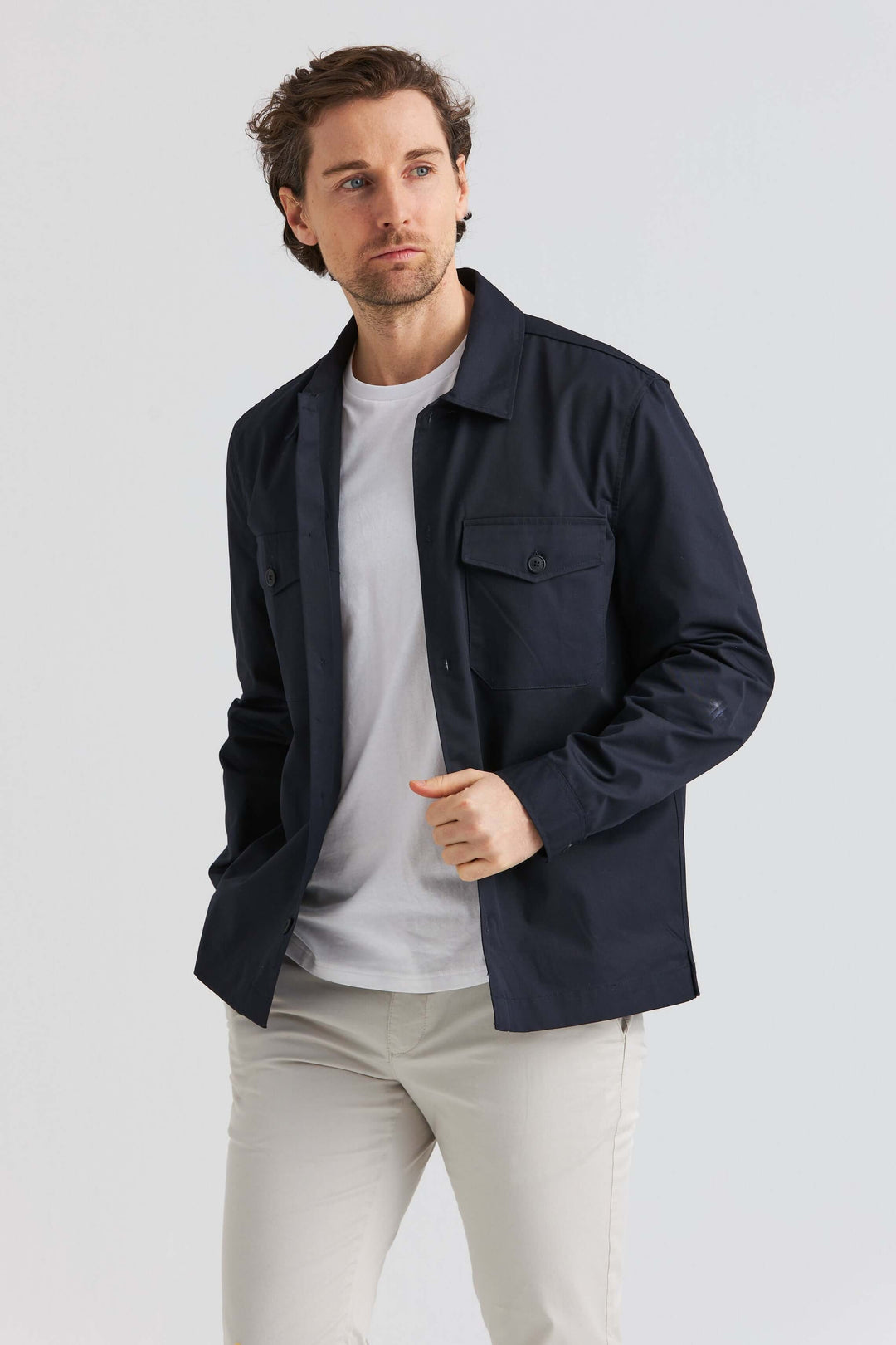 Marinblå City Overshirt på en man som poserar, bär en marinblå overshirt med diskreta detaljer och vita byxor.