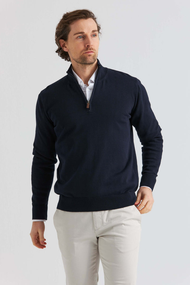 Marinblå bomullströja half zip på en man, stilren med krage och halv dragkedja, bärs med ljusa byxor.