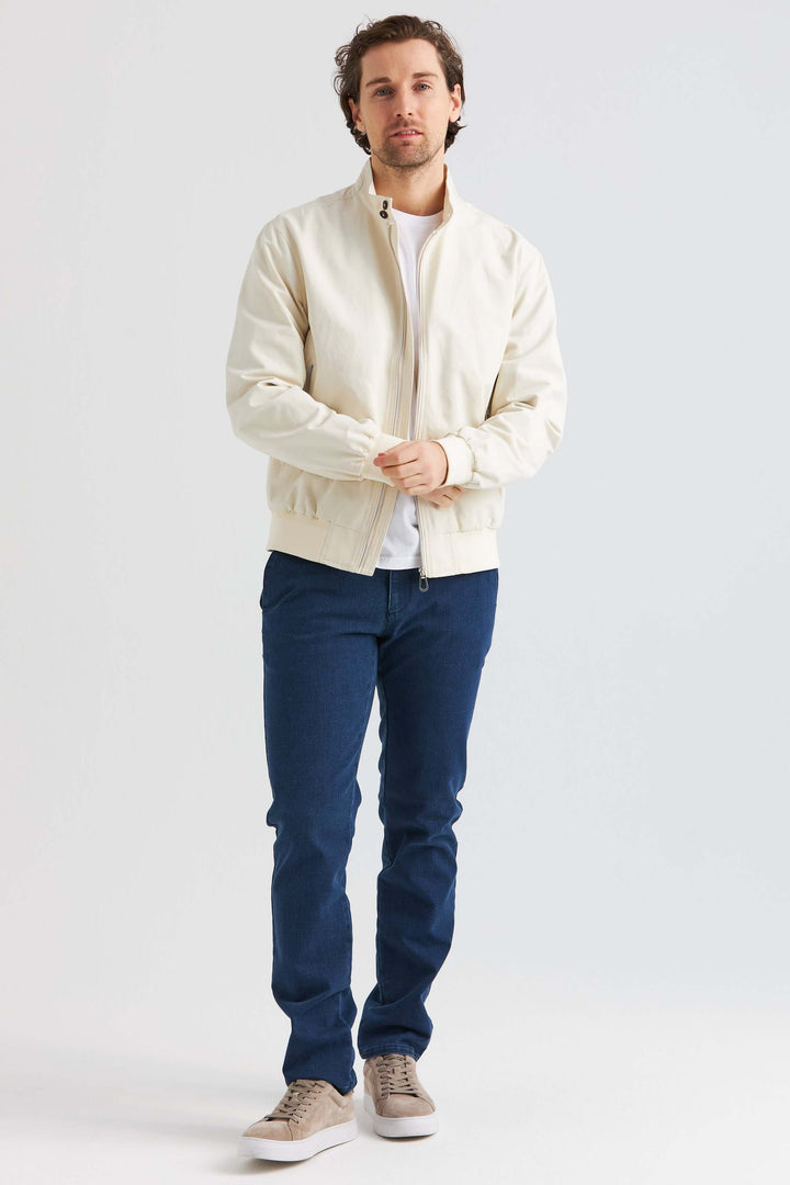 Man wearing beige vårjacka i bomullsblandning with blue jeans and sneakers in a bright setting.