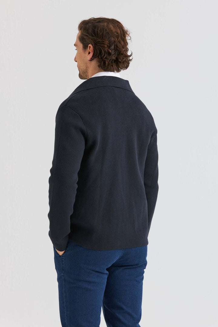 Man i marinblå stickad overshirt sedd bakifrån, bärandes blå byxor.