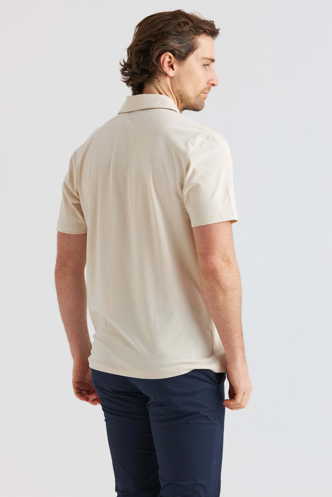 Man visar en Beige Pikétröja från sidan, med korta ärmar och en avslappnad passform.