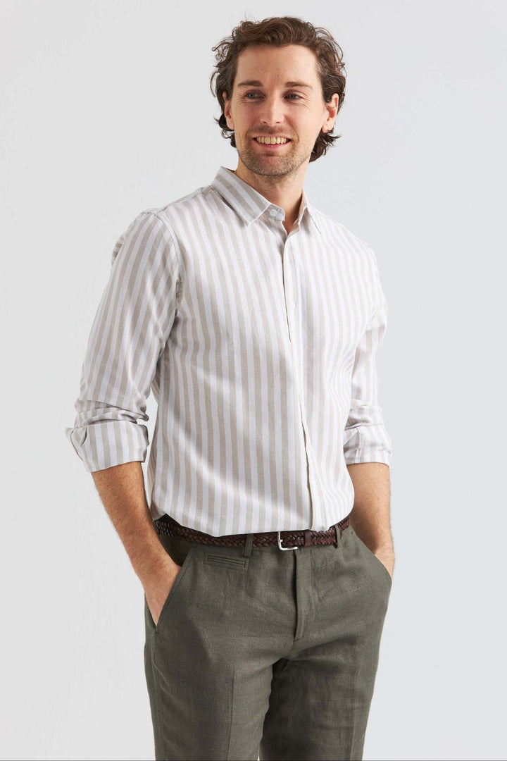 Beige randig linneskjorta på en man med leende och händerna i fickorna, stilren och bekväm för varmare dagar.