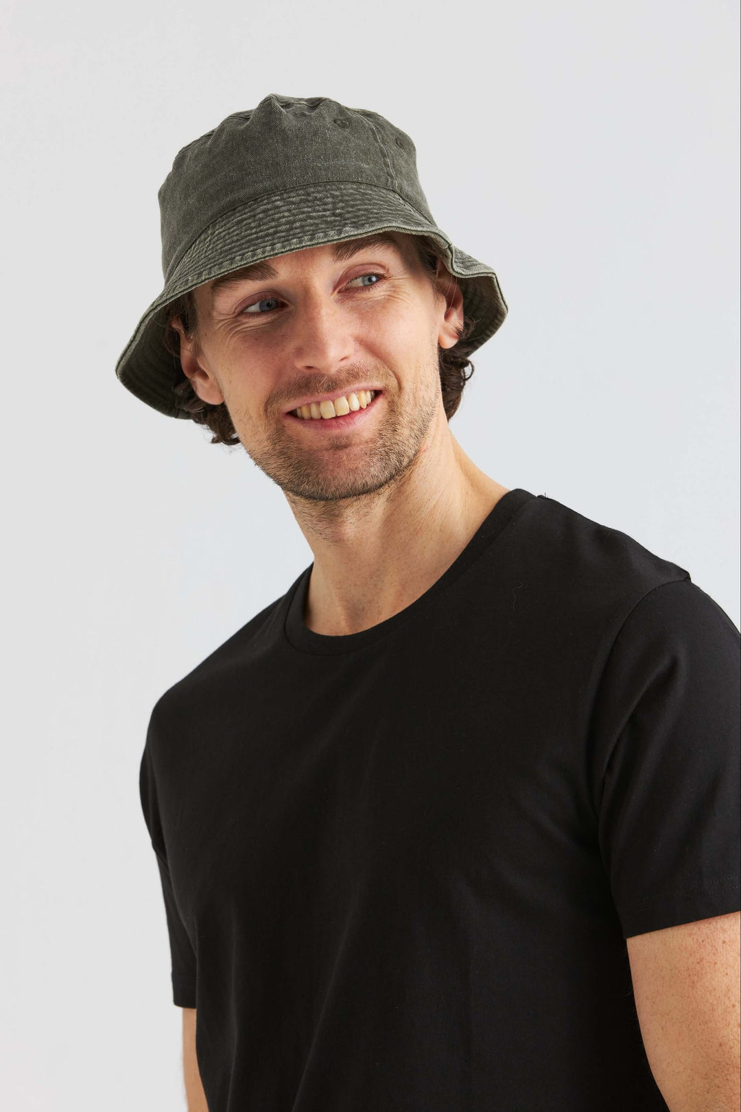 Grön Bucket Hat Washed Cotton på en man som bär en svart t-shirt och ler.
