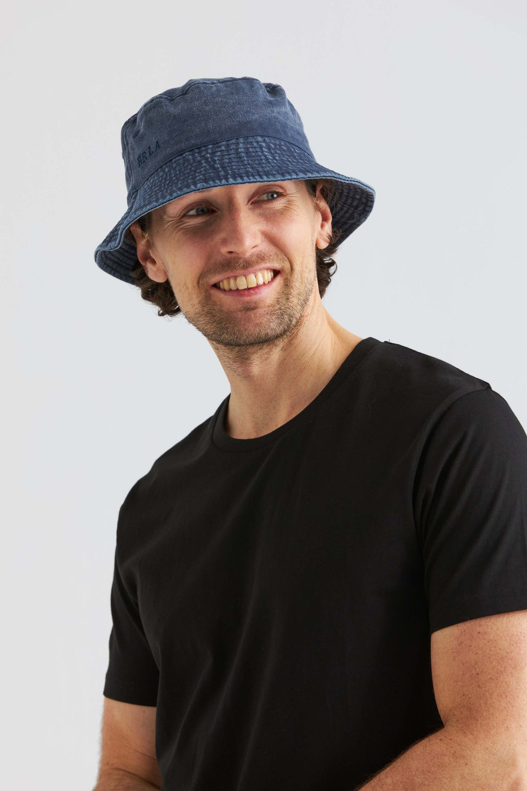 Blå Bucket Hat Washed Cotton på man med svart tröja och leende, perfekt som sommaraccessoar
