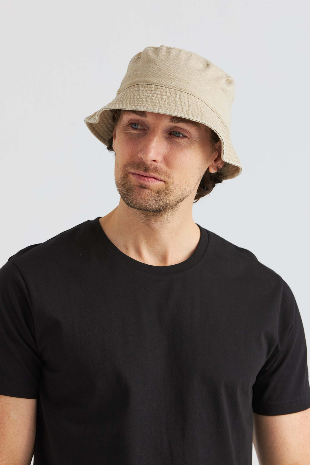 Man wearing a beige bucket hat made of washed cotton, paired with a black T-shirt, stylish summer accessory.