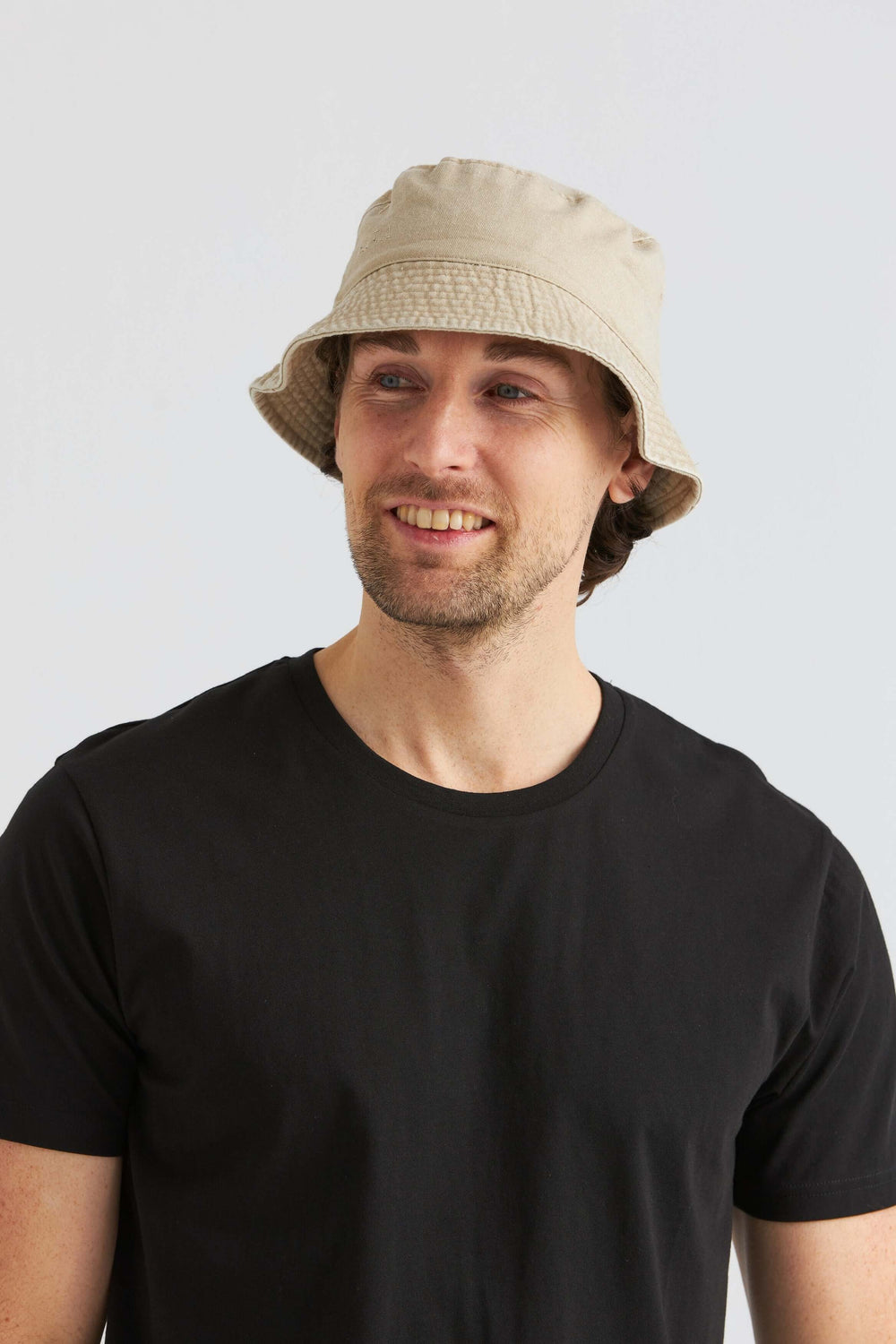 Man wearing a beige bucket hat made of washed cotton, styled with a black t-shirt, perfect summer accessory.