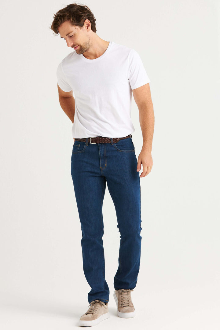 Man som bär 4500 jeans stretch mellanblå tillsammans med en vit t-shirt, poserar för en bild.