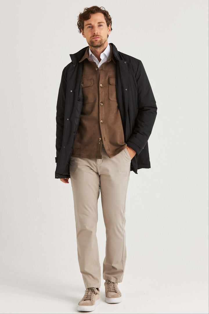 Man wearing a Brun Suede Overshirt with large pockets and a black jacket, styled with beige pants.