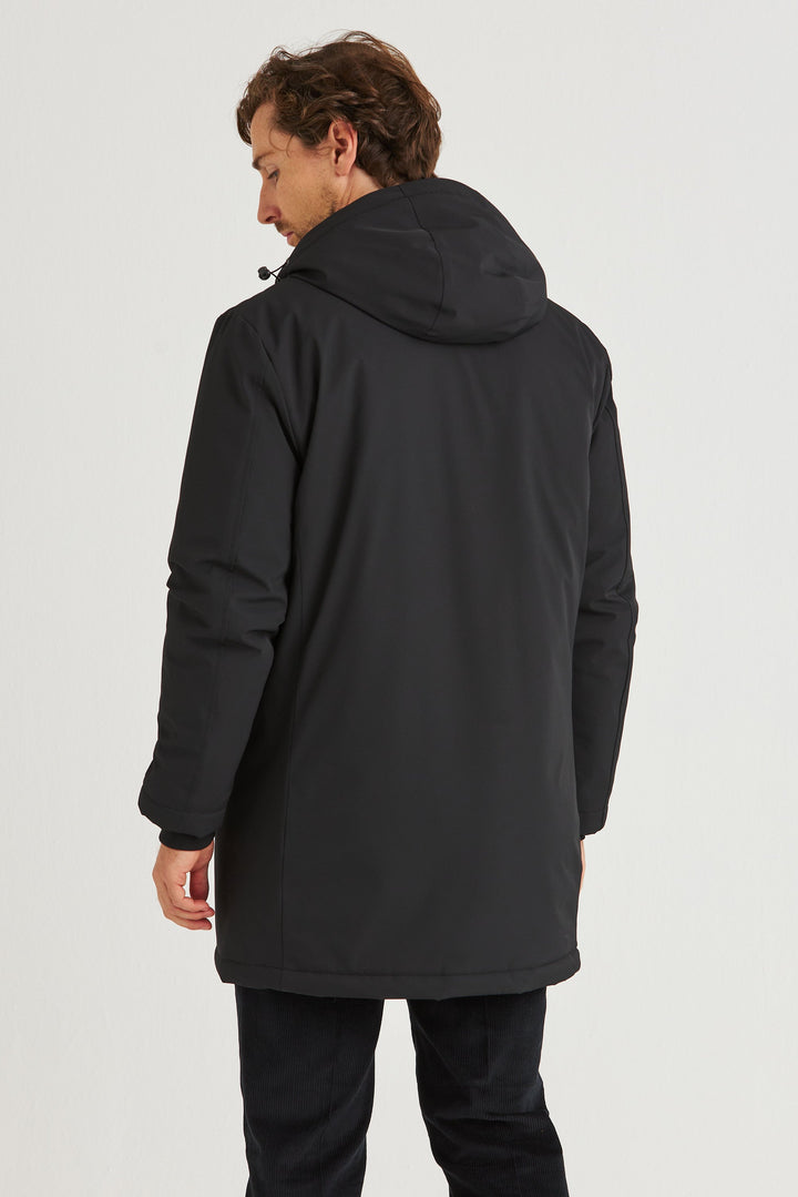 Man wearing a Svart Lång Cityjacka, showing the back view with hood, ideal for colder days.