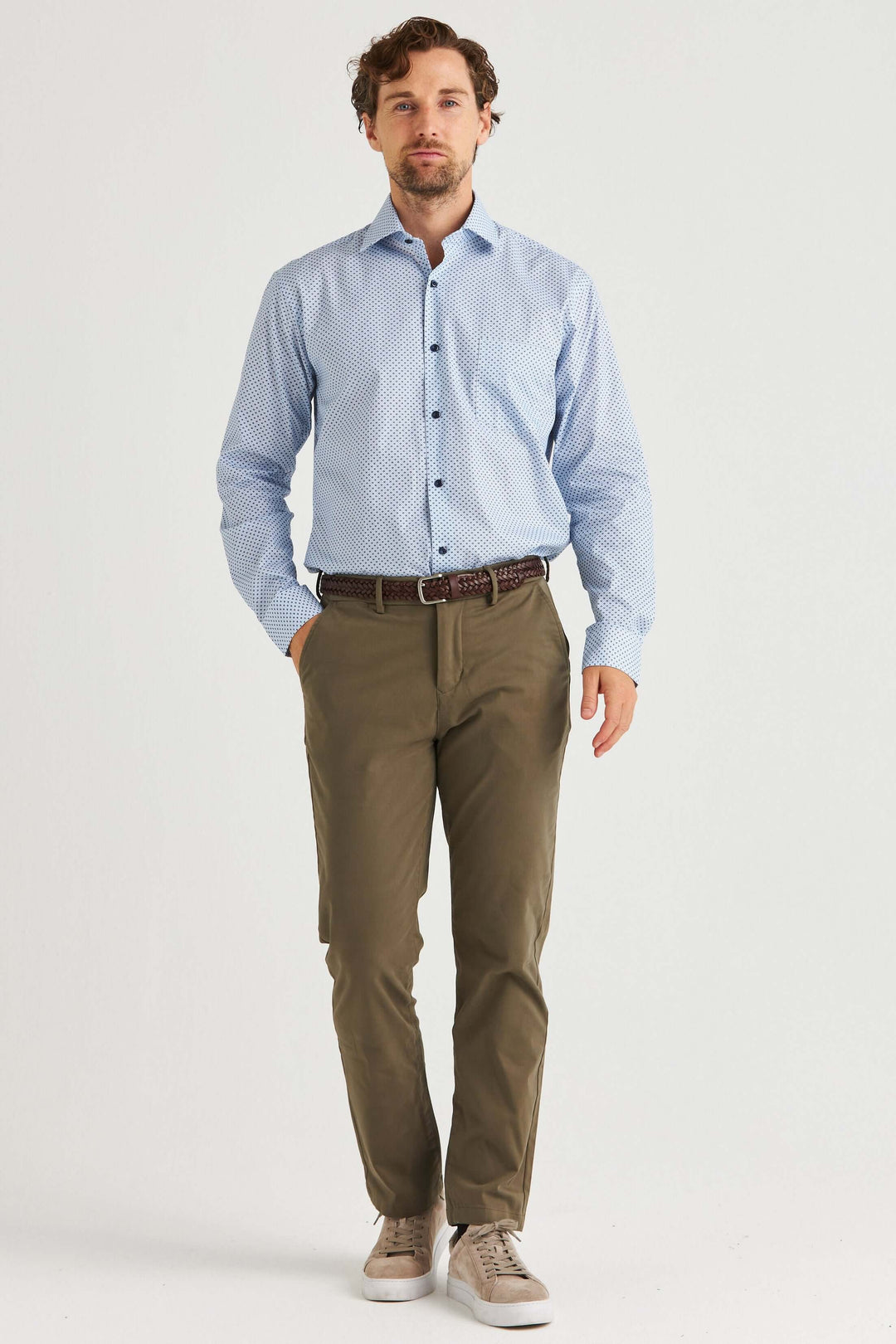 Man i ljusblå skjorta med småmönster och olivgröna byxor, stilren och modern outfit.