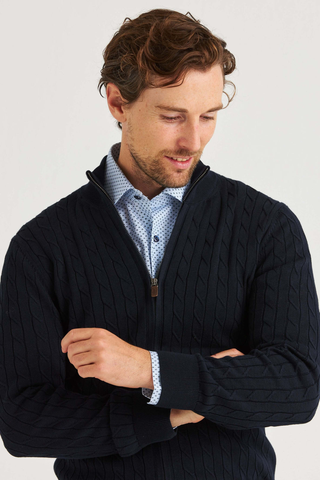 Marinblå Kabelstickad Full Zip ifrån en man som bär den över en mönstrad skjorta.