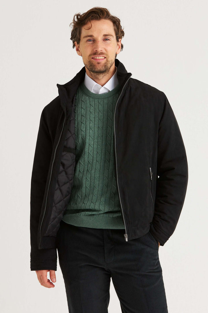 Man som bär en svart jacka över en grön tröja, med en stilren och klassisk design.