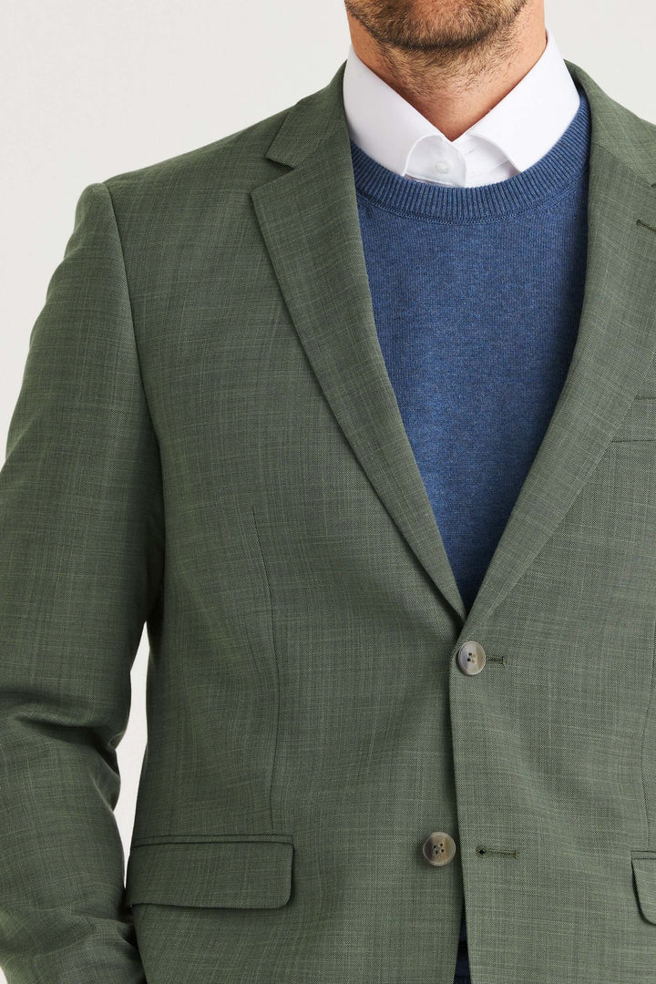 En man bär en Grön Kavaj med en blå tröja under, vilket ger en modern och stilren look.