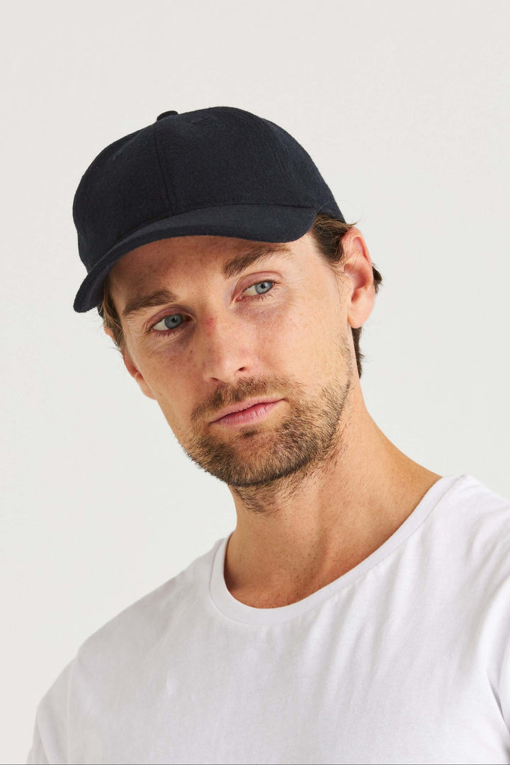 Marinblå Keps Wool Look på en man med kort hår, iförd en vit t-shirt, med ett seriöst uttryck.