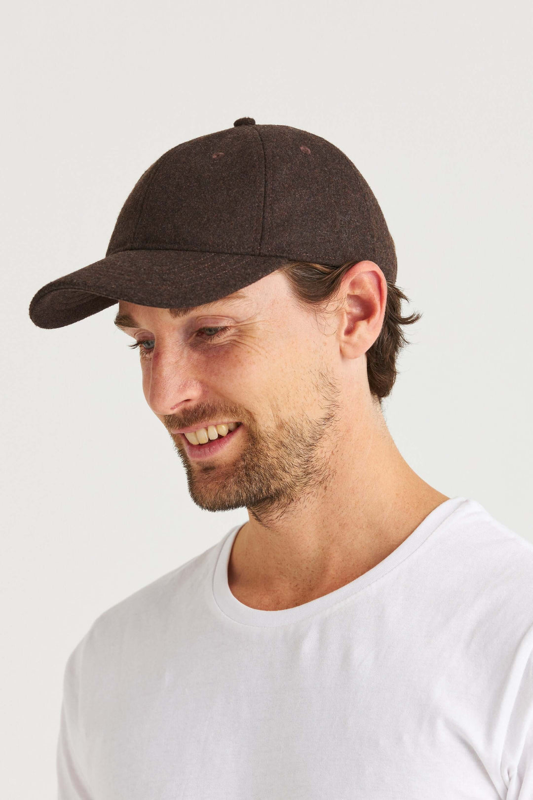 Brun Keps Wool Look på en man som bär en vit t-shirt och ler, med en mjuk ullinspirerad design.